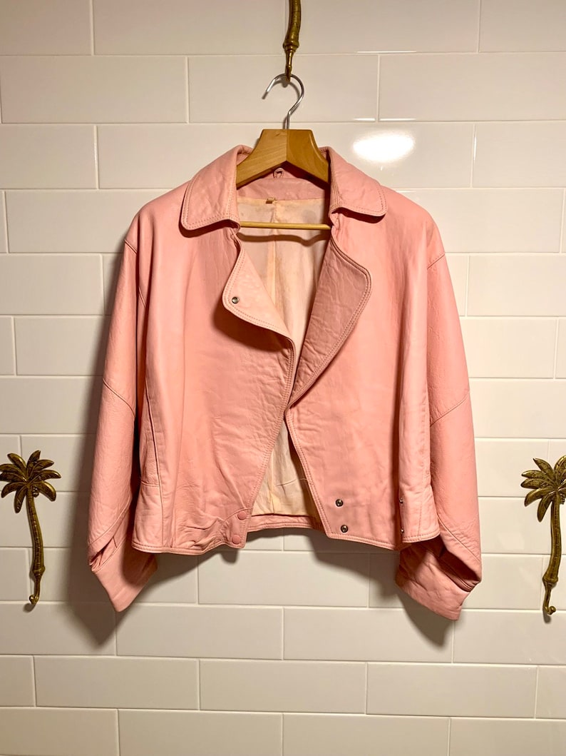 Puede incluir: Una chaqueta de cuero rosa con cierre de cremallera y mangas largas. La chaqueta tiene un estilo motero cl&aacute;sico con un corte ligeramente recortado.
