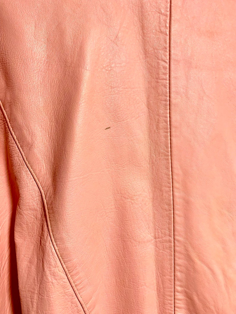 Puede incluir: Primer plano de una chaqueta de cuero rosa p&aacute;lido con una costura en la espalda.