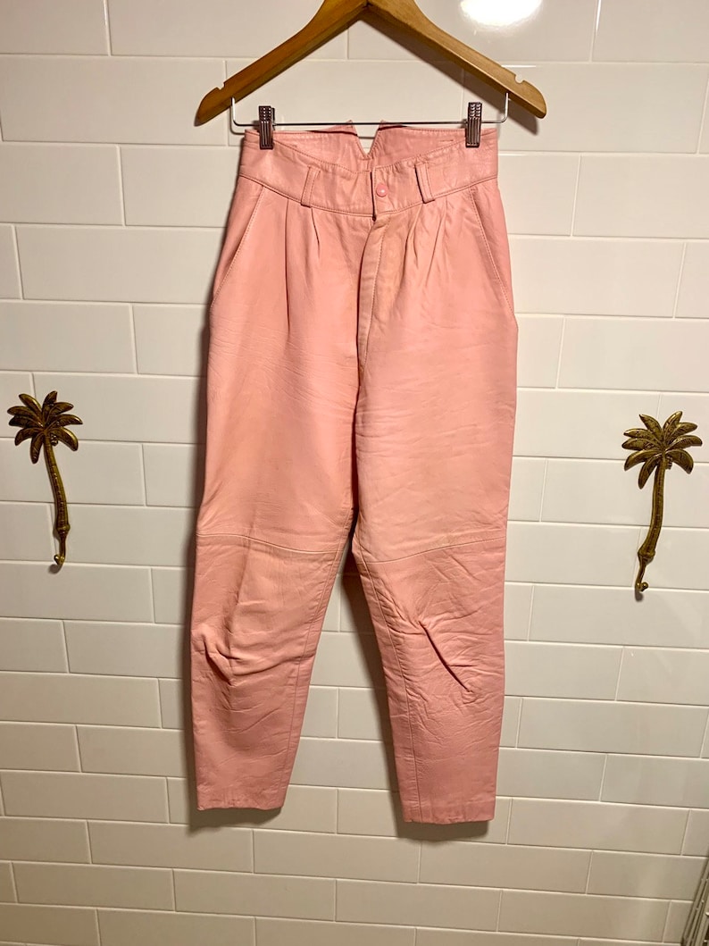 Puede incluir: Pantal&oacute;n de cuero rosa de cintura alta con cierre de bot&oacute;n. El pantal&oacute;n tiene una pierna recta y est&aacute; hecho de cuero suave y flexible.