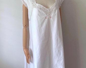 Puede incluir: Un camisón de algodón blanco con mangas cortas y escote cuadrado adornado con encaje blanco intrincado. La prenda incluye pequeñas iniciales rojas bordadas "GM" centradas debajo del escote en la zona del pecho frontal.