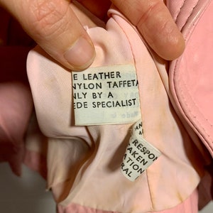 Puede incluir: Primer plano del forro interior de una chaqueta de cuero rosa con una etiqueta de cuidado blanca que dice "E Leather Nylon Taffeta Only By A Ede Specialist".