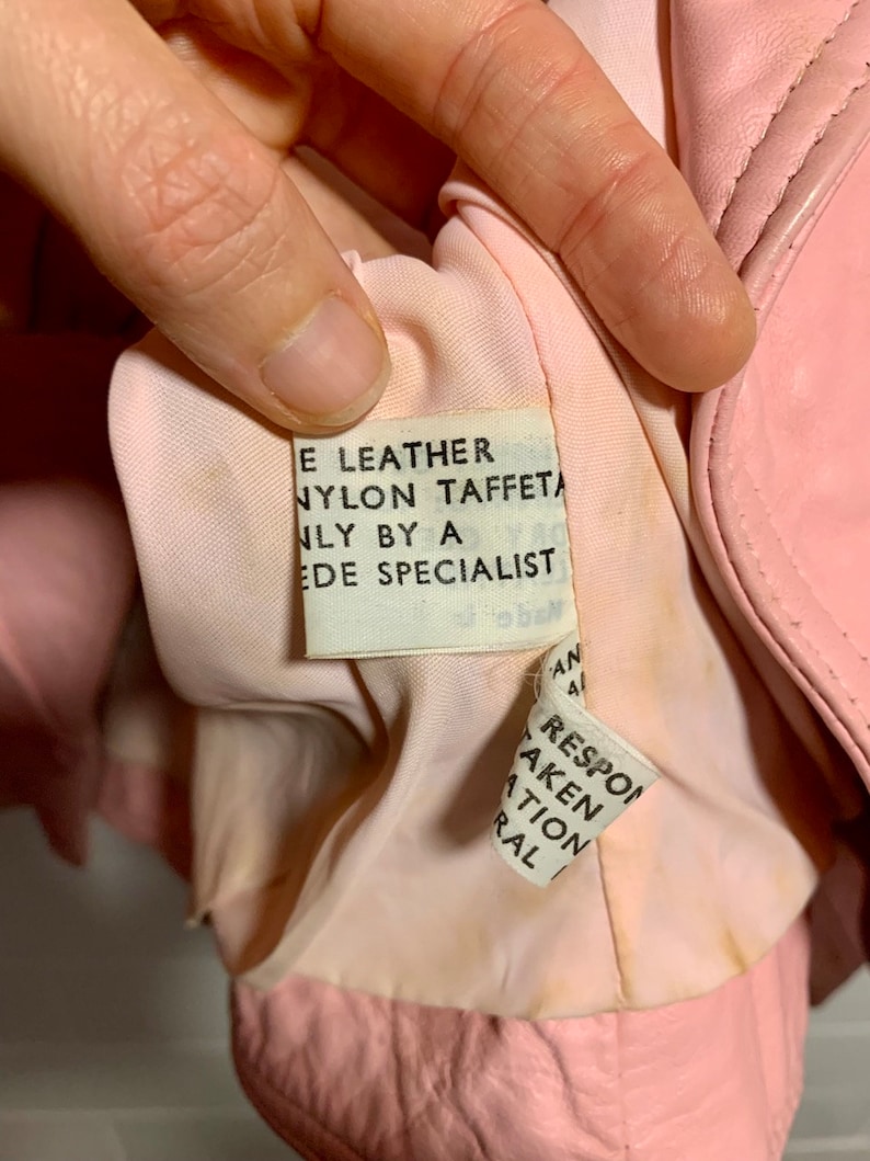 Puede incluir: Primer plano del forro interior de una chaqueta de cuero rosa con una etiqueta de cuidado blanca que dice "E Leather Nylon Taffeta Only By A Ede Specialist".