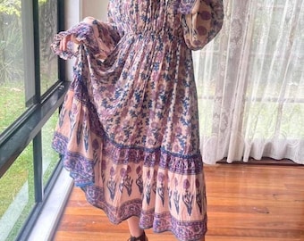 Puede incluir: Un vestido largo y fluido con un estampado floral en tonos rosa, morado y azul. El vestido presenta mangas largas, un escote cuadrado y cintura elástica. El dobladillo está adornado con un borde decorativo. El texto en la parte inferior de la imagen dice "dress from circa /us pas elastic waist to cinco for extra".