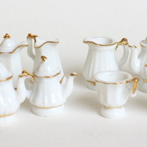 Puede incluir: Un juego de diez teteras y jarras de crema en miniatura de porcelana blanca con detalles dorados. Las teteras y las jarras de crema son de diferentes formas y tamaños.