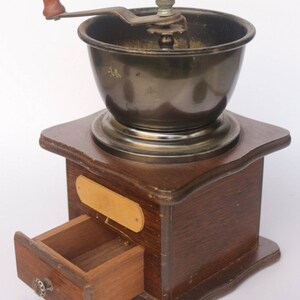 May include: A vintage wooden coffee grinder with a metal grinder and a wooden drawer. The grinder has a crank handle and a metal base.
