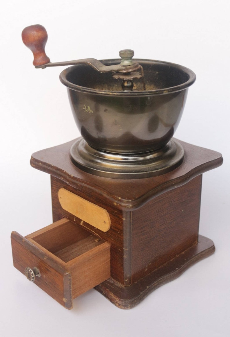 May include: A vintage wooden coffee grinder with a metal grinder and a wooden drawer. The grinder has a crank handle and a metal base.