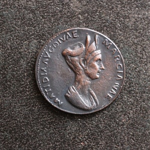 Puede incluir: Una moneda de bronce con un retrato de una mujer con una corona y la inscripción "MATIDIA AVG DIVAE MARCIANAE" alrededor del borde.
