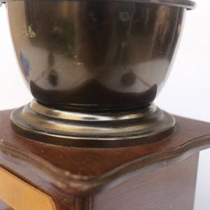 May include: A vintage wooden coffee grinder with a dark brown base and a silver metal top. The grinder has a large, round, silver metal bowl.