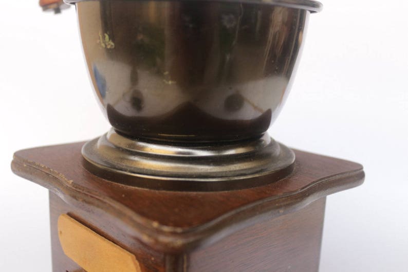 May include: A vintage wooden coffee grinder with a dark brown base and a silver metal top. The grinder has a large, round, silver metal bowl.