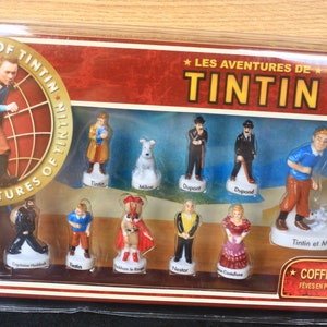 May include: A collector's set of porcelain figurines featuring characters from "The Adventures of Tintin." The set includes Tintin, Snowy, Captain Haddock, and other characters. The box has the title "Les Aventures de Tintin."