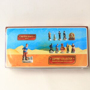 May include: A collector's box featuring miniature porcelain figurines. The box has a blue background with various characters and the text "COFFRET COLLECTOR". The figurines include Tintin and Snowy, and other characters.