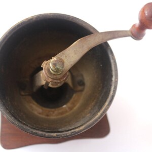 May include: A vintage wooden coffee grinder with a metal crank and a dark brown wooden base.