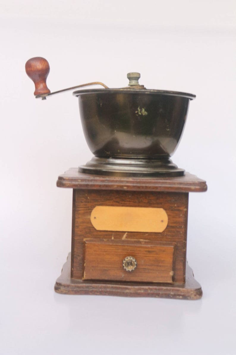 May include: A vintage wooden coffee grinder with a black metal grinder and a wooden crank handle. The grinder has a small drawer on the front.