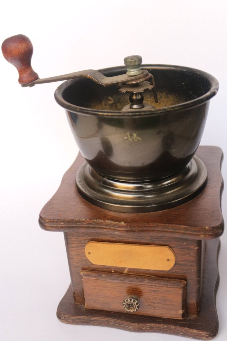 May include: A vintage wooden coffee grinder with a metal crank and a drawer for collecting coffee grounds. The grinder has a dark brown wooden base and a metal top with a black interior.