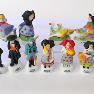 Puede incluir: Colecci&oacute;n de figuras de cer&aacute;mica que representan a personas con trajes tradicionales europeos. Las figuras son de colores brillantes y presentan detalles como sombreros, delantales y cestas. Algunas figuras sostienen gansos u otros objetos. Cada figura est&aacute; sobre una base blanca.