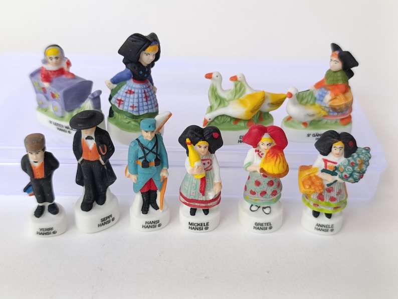 Puede incluir: Colecci&oacute;n de figuras de cer&aacute;mica que representan a personas con trajes tradicionales europeos. Las figuras son de colores brillantes y presentan detalles como sombreros, delantales y cestas. Algunas figuras sostienen gansos u otros objetos. Cada figura est&aacute; sobre una base blanca.