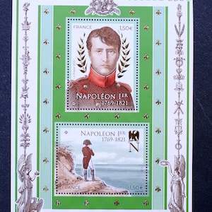 Könnte beinhalten: Zwei Briefmarken mit Napoleon Bonaparte. Die obere Marke zeigt ein Porträt von Napoleon in roter Uniform mit einem goldenen Lorbeerkranz. Die untere Marke zeigt Napoleon, der auf einer Klippe steht und auf das Meer blickt. Beide Marken sind grün mit goldenen Akzenten und tragen den Text "Napoleon Ier 1769-1821".