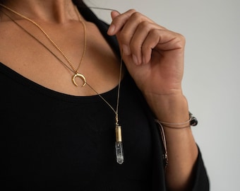 May include: A layered necklace with a gold crescent moon pendant and a clear crystal pendant on a gold chain.
