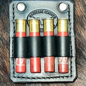 May include: Black leather shotgun shell holder with four slots. The holder has the text "HARDCORE LEATHER" embossed on the front.