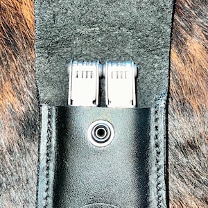 May include: Black leather pouch with a snap closure and a stitched design. The pouch is open and shows two silver multi-tools inside. The pouch has a logo that says "Winston Heart Products of TX".
