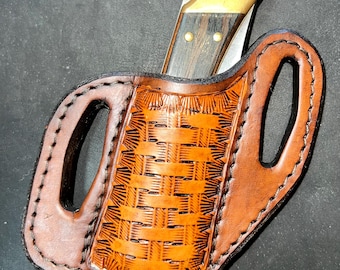 May include: A brown leather knife sheath with a woven pattern and two belt loops. A folding knife with a wood handle and brass accents is inside the sheath.