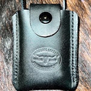 May include: A black leather case with a snap closure and a stitched border. The case has a logo that reads "True Core Leather" with the words "Handcrafted" and "Hoban" underneath.