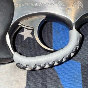 May include: Close-up of a silver Ruger Redhawk revolver. The trigger guard is wrapped in a white and black braided material. The background is a blue and black patterned fabric with a white star.