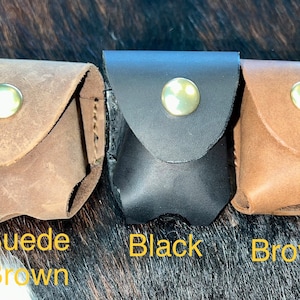 May include: Three leather cases for small items, such as Airpods. The cases are in suede brown, black, and brown leather. Each case has a brass button closure.