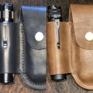 May include: Two leather flashlight holsters, one black and one brown, with a flashlight in each. The holsters have a snap closure and a belt loop.