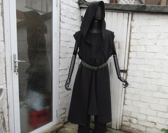 May include: A black hooded cloak and matching pants are displayed on a mannequin. The cloak has a textured pattern and is cinched at the waist with a green belt. The mannequin stands in front of a white brick wall and a white door.
