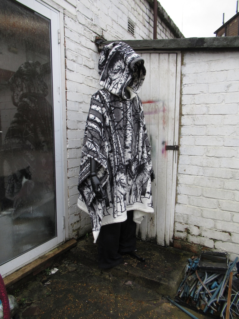 May include: A hooded poncho with a black and white pattern of trees and animals. The poncho is made of a soft, fuzzy fabric and has a drawstring hood.