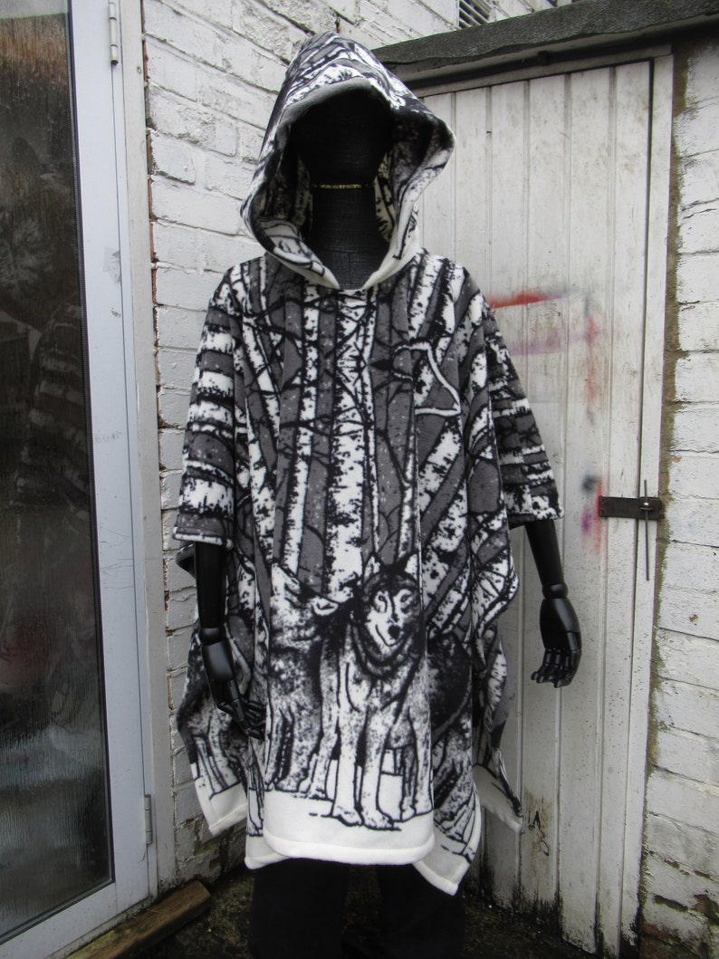 May include: A white and gray hooded poncho with a wolf print. The poncho has a black and white forest scene with trees and wolves.