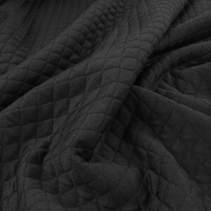 May include: Close-up of black quilted fabric with a diamond pattern. The fabric is draped, showing the texture and depth of the material. The dark color and pattern suggest a cozy or decorative textile.