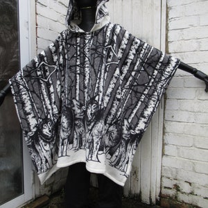 May include: A white hooded poncho with a black and white wolf and birch tree print. The poncho is made of a soft, fuzzy material.
