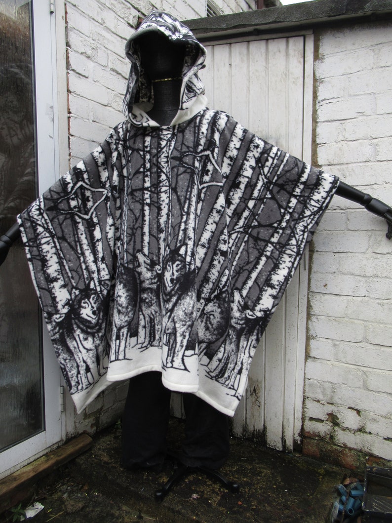 May include: A white hooded poncho with a black and white wolf and birch tree print. The poncho is made of a soft, fuzzy material.