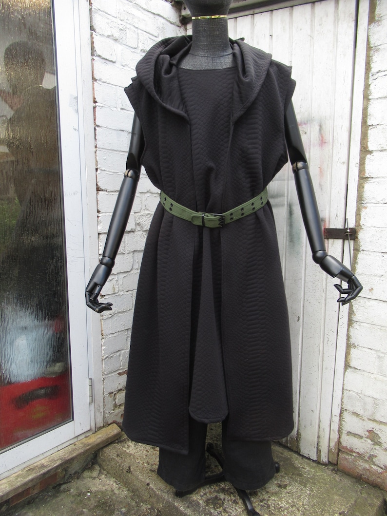 May include: A black hooded coat and matching pants are displayed on a mannequin. The coat features a quilted texture, a draped front, and a green belt. The outfit is styled on a black mannequin with articulated arms and hands.