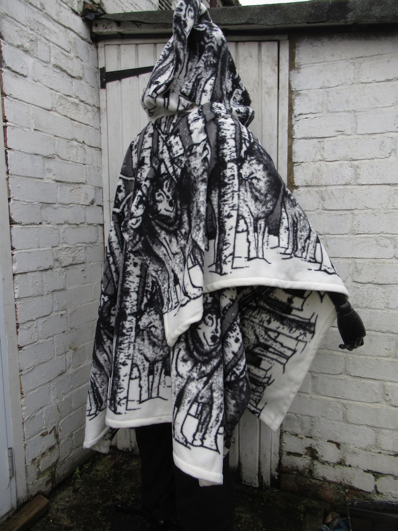 May include: A white hooded fleece blanket with a black and white print of trees and wolves. The blanket is folded in half and draped over a person's shoulders.