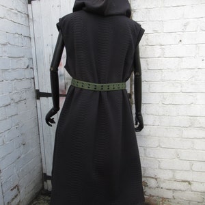 May include: A black hooded vest with a textured pattern, sleeveless design, and a matching black belt. The vest is long, reaching the ankles, and is displayed on a mannequin. The belt is olive green with evenly spaced holes.