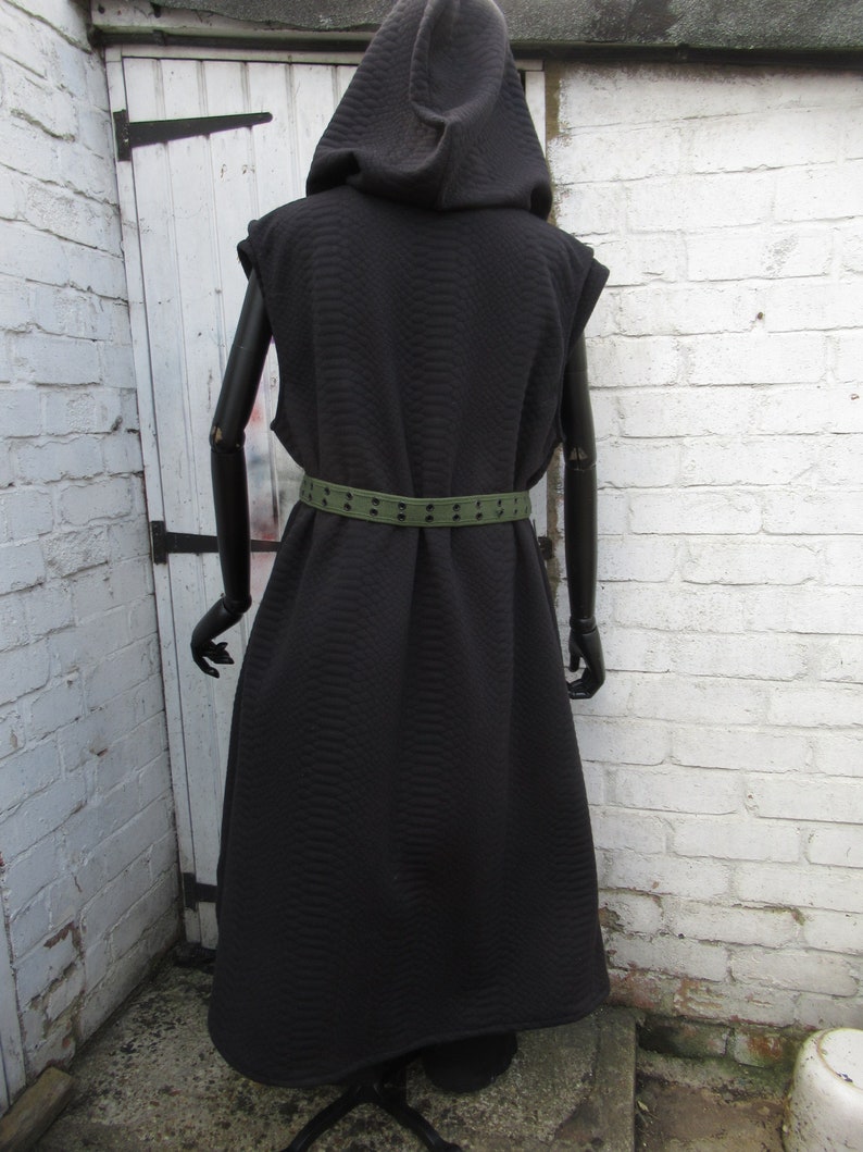 May include: A black hooded vest with a textured pattern, sleeveless design, and a matching black belt. The vest is long, reaching the ankles, and is displayed on a mannequin. The belt is olive green with evenly spaced holes.