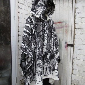 May include: A hooded poncho with a black and white forest print featuring trees and wolves. The poncho is made of a soft, fleece-like material.