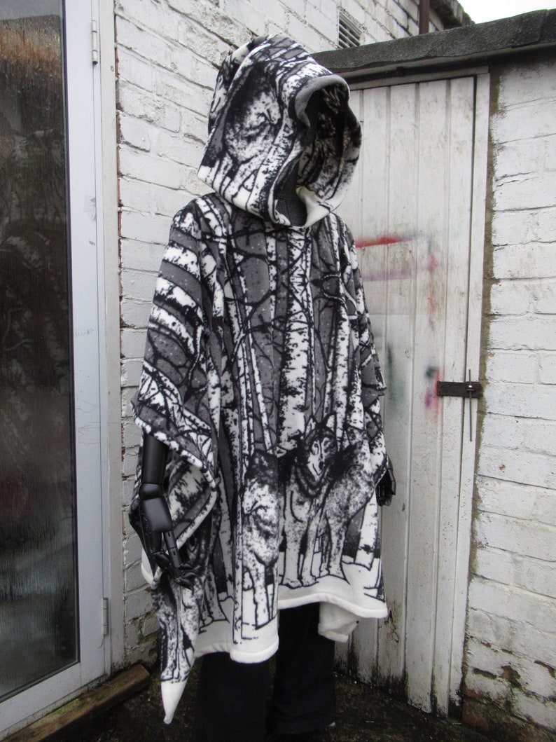 May include: A hooded poncho with a black and white forest print featuring trees and wolves. The poncho is made of a soft, fleece-like material.
