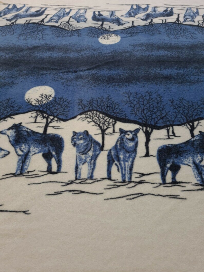 May include: A white and blue fleece blanket with a design of wolves howling at the moon. The blanket features a white background with a blue sky and trees. The wolves are blue and white.
