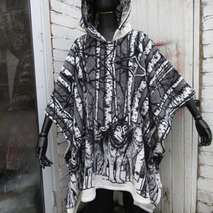 May include: A hooded poncho with a black and white woodland print featuring trees and wolves. The poncho is made of a soft, fleece-like material.