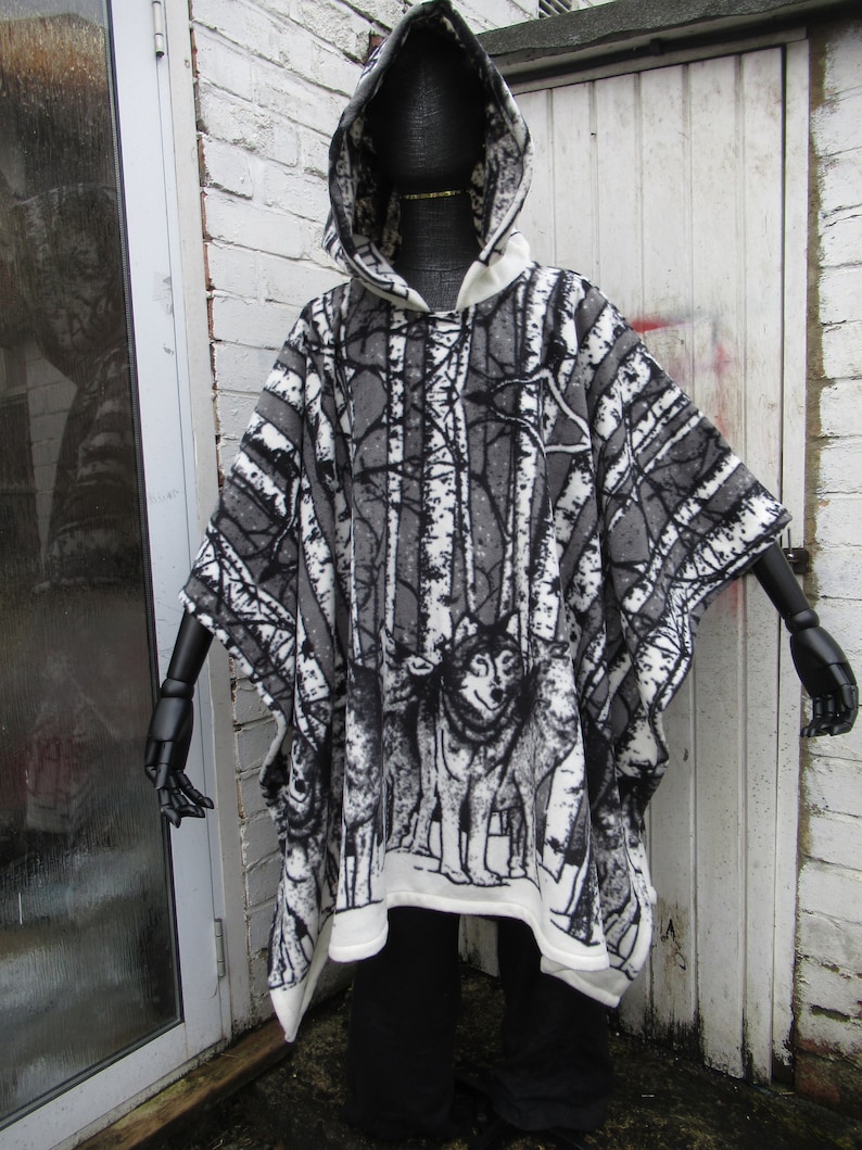 May include: A hooded poncho with a black and white woodland print featuring trees and wolves. The poncho is made of a soft, fleece-like material.