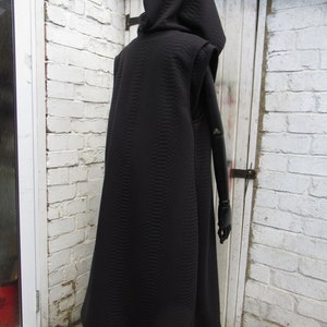 May include: A black hooded cloak with a quilted pattern. The cloak has a sleeveless design and a long, flowing skirt. The hood is large and covers the head. The cloak is displayed on a black mannequin arm.