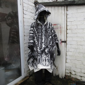 May include: A black and white hooded poncho with a forest scene print. The poncho is made of a soft, fuzzy fabric and has a drawstring hood.