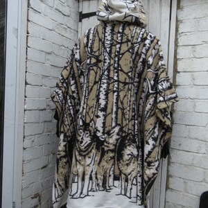 May include: A hooded fleece poncho with a white background and a black and brown print of trees and wolves. The poncho has a white hood and a brown fleece lining.