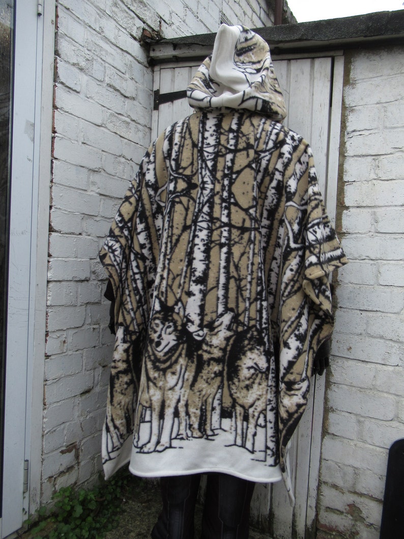 May include: A hooded fleece poncho with a white background and a black and brown print of trees and wolves. The poncho has a white hood and a brown fleece lining.
