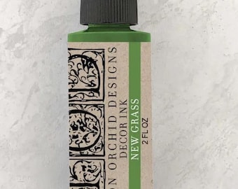 May include: A 2 fl oz bottle of Iron Orchid Designs Decor Ink in the color New Grass. The bottle is green with a black cap and a label with the company name and product details.