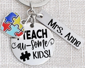 May include: A silver keychain with a round charm that says "I Teach Au-some Kids!" with a black puzzle piece. There is a small heart-shaped charm with a colourful puzzle piece design and a silver tag that says "Mrs. Anne".